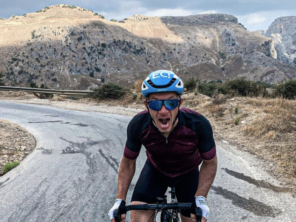 falko krismayr network marketing expert riding a bike down a road with mountains in the background.
