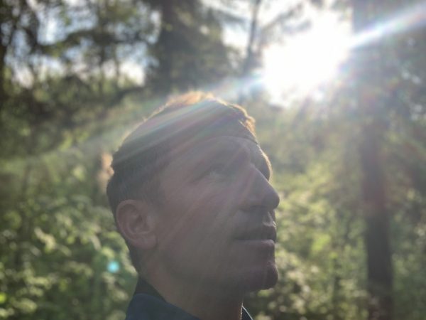 falko krismayr network marketing expert standing in a forest with the sun shining through the trees.